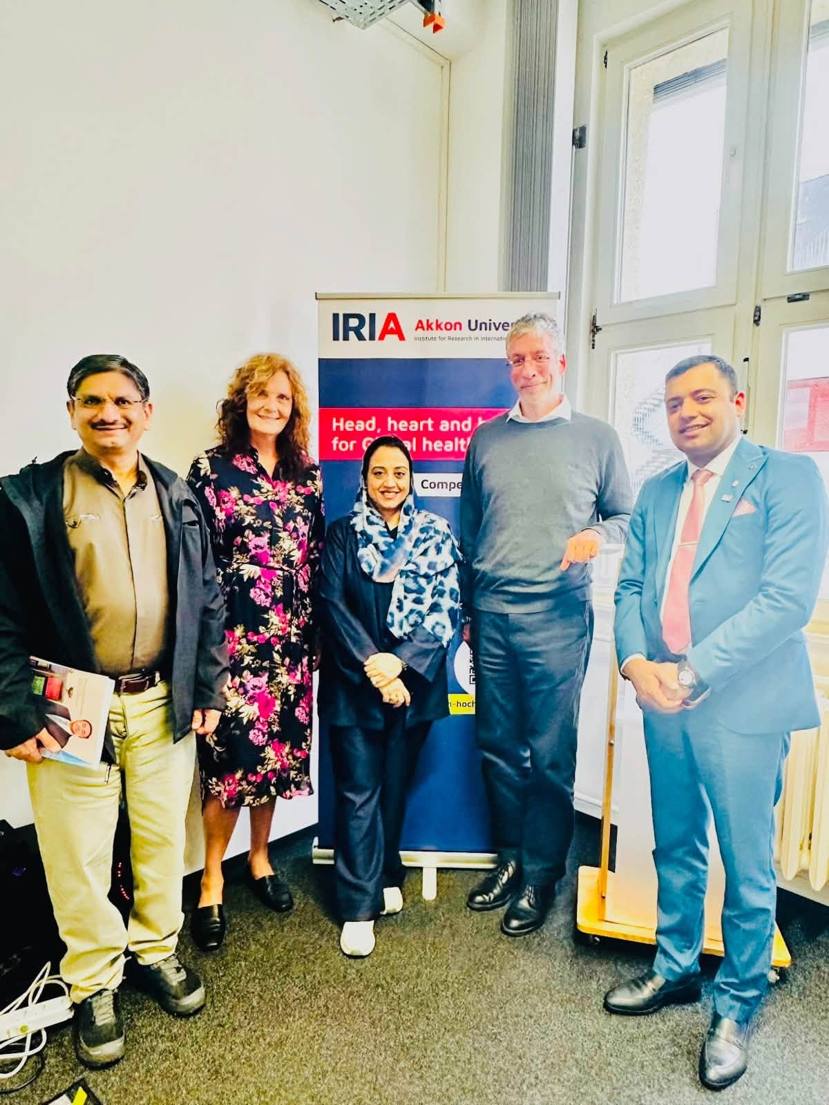 Dr. Farhat Asif with colleagues in front of the IRIA Akkon University banner in Berlin
