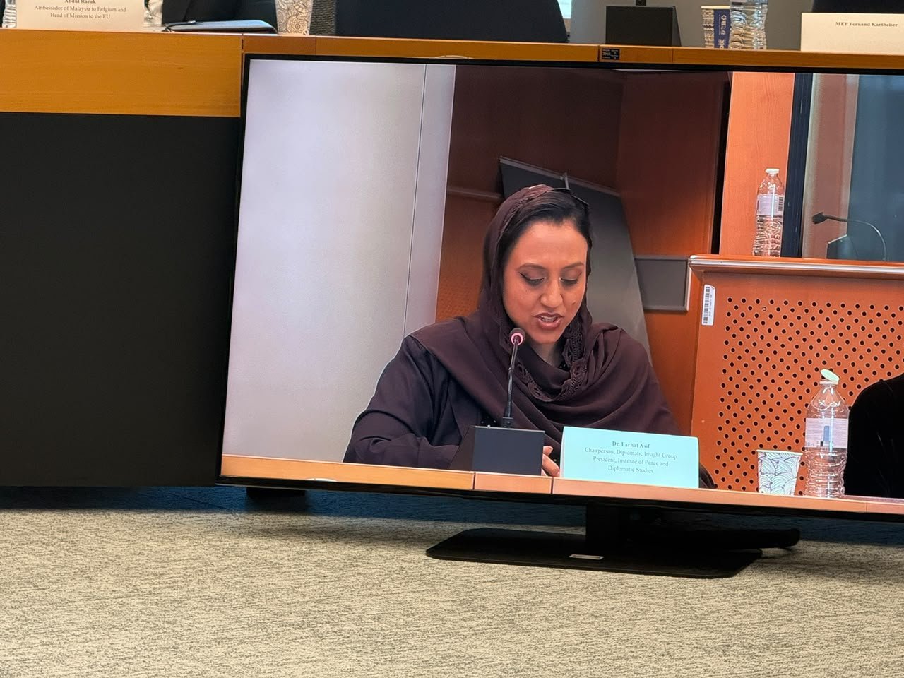 Dr. Farhat Asif speaking, shown on the screen in the European Parliament meeting room